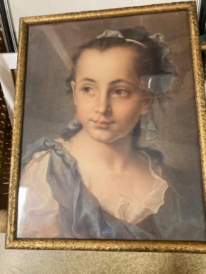 Inramad porträttmålning i guldram - Säljer en klassisk porträttmålning av en ung kvinna, inramad i en dekorativ guldfärgad ram med detaljerade mönster. Tavlan har mjuka färger i blått, vitt och beige och är skyddad av glas. Perfekt som väggdekoration för dig som gillar konst och vintage. Ramen är från början av 1900- talet. 