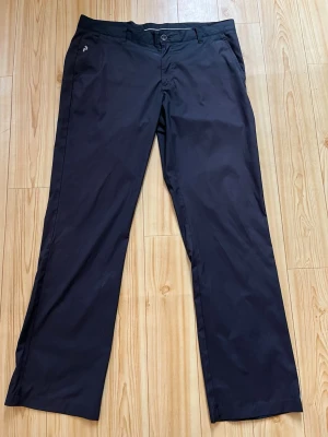 Peakperformance golfbyxor  - Snygga svarta chinos med raka ben och klassisk passform. Byxorna har sidofickor, bälteshällor och stängs med knapp och dragkedja. Materialet ser ut att vara bomull eller en bomullsblandning som ger en stilren look.