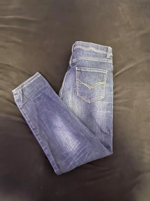 Mörkblå raka jeans med kontrastsöm - Snygga mörkblå jeans med raka ben och klassisk femficksmodell. Jeansen har kontrastsömmar på bakfickorna och lätt slitna detaljer framtill och baktill. Perfekta till en avslappnad streetwear-look.