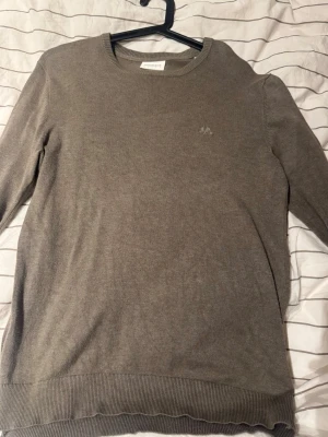 Beige stickad tröja från Lindbergh - Snygg beige stickad tröja från Lindbergh med rund halsringning och diskret logga på bröstet. Tröjan har långa ärmar och ribbade muddar vid ärmslut och nederkant. Perfekt för lager på lager och enkel att matcha.