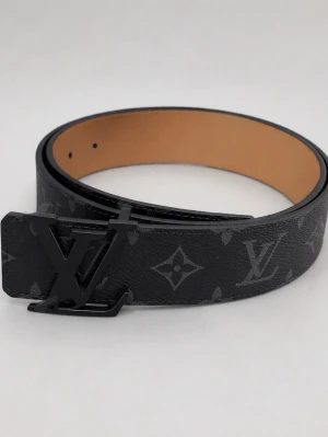 Svart LV-bälte  - Snyggt svart LV-bälte med klassiskt monogrammönster och stor LV-logga på spännet. Bältet har en stilren design och är gjort i skinn med en beige insida. Perfekt accessoar för att lyfta din outfit.