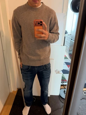 Beige stickad tröja från Bläck - En enkel och stilren beigebrun stickad tröja med rund halsringning och ribbade muddar vid ärmslut och nederkant. Perfekt för lager på lager och passar till det mesta. Tröjan har en avslappnad passform och är gjord i mjukt material.