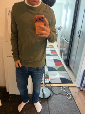 Olivgrön basic tröja - En enkel och stilren olivgrön tröja med rund halsringning och långa ärmar. Tröjan har ribbade muddar vid ärmslut och nederkant. Perfekt att matcha med jeans för en avslappnad look. Storlek L från selected homme knappt använd