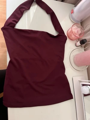 Mörkröd one shoulder topp - Snygg mörkröd one shoulder topp med bred axelrem. Toppen är ärmlös och har en tight passform, perfekt för att lyfta din stil. Tillverkad i mjukt material som känns skönt mot huden.