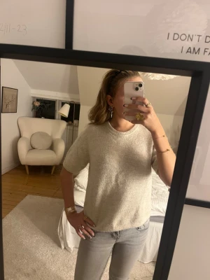 Beige stickad t-shirt - Mysig beige stickad t-shirt med korta ärmar och rund hals. Tröjan har en avslappnad passform och är gjord i ett mjukt material som ser ut att vara en ull- eller bomullsblandning. Perfekt att styla med jeans för en enkel look och inför hösten 🤎