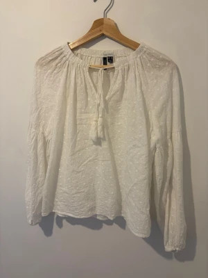 Vit boho-blus med knytband - Säljer en vit blus i boho-stil med broderade detaljer och knytband med tofsar vid halsen. Blusen har lång ärm och är gjord i ett lätt, luftigt tyg som ger en avslappnad look. Perfekt till jeans eller kjol för en trendig outfit.