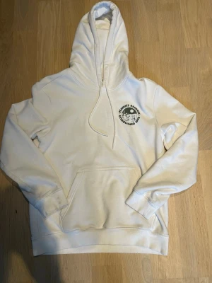 Vit hoodie med Peanuts Records-tryck - Säljer en vit hoodie med stor ficka framtill och huva med dragsko. På bröstet finns ett litet svart tryck med texten 'Peanuts Records Established 1950' och på ryggen ett stort tryck med samma tema och motiv från Peanuts. Mjuk och skön bomullskänsla.