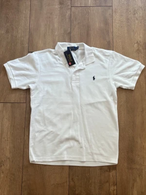 Helt ny Ralph Lauren Polo Shirt (Vit) - Strl M 🐎✨ - Säljer en klassisk vit pikétröja från Ralph Lauren i absolut nyskick. Den är helt oanvänd med tags kvar och kommer i originalpåse. En riktig klassiker som passar till allt!  Märke: Polo Ralph Lauren  Storlek: M  Färg: Vit med mörkblå logga  Skick: Helt ny / Deadstock (DS) med tags Skickas spårbart eller hämtas enligt överenskommelse. Hör av dig i DM om du har några frågor! 🤝 