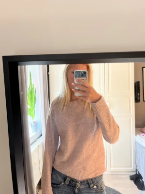 Ljusrosa stickad tröja - Mysig ljusrosa stickad tröja med rund halsringning och långa ärmar. Tröjan har ribbade muddar vid ärmslut och nederkant, vilket ger en avslappnad och stilren look. Perfekt för kyligare dagar och enkel att matcha med jeans eller kjol.