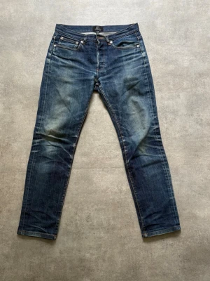 APC jeans - Säljer ett par klassiska blå jeans med raka ben och snygga slitningar på framsidan. Jeansen har fem fickor, knappgylf och kontrastsömmar. Perfekta till en avslappnad stil och tillverkade i denim.