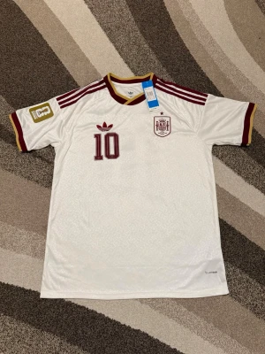 Spanien 2026 Bortatröja  - Spanien 2026 Bortatröja Storlek: XXL Namn och nummer: Lamine Yamal 10 Badge: VM Beskrivning: Tröjan är helt ny men har fel nummer. De ska igenkligen va nr 19 men de har tryckts 10 istället. 
