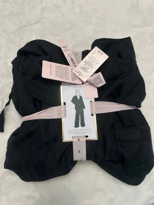 Svart satinpyjamas från Victoria's Secret - Helt ny, endast testad. Snygg svart pyjamas i satin från Victoria's Secret Signature. Setet består av långärmad skjorta och byxor med avslappnad passform. Materialet är glansigt och mjukt, perfekt för mysiga kvällar hemma. Storlek xs. 