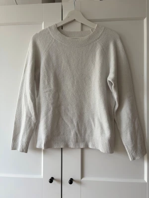 Vit stickad tröja från Vero Moda - Klassisk vit stickad tröja från Vero Moda med rund halsringning och ribbade muddar vid ärmslut och nederkant. Tröjan har en enkel och stilren design som passar till det mesta. Tröjan är nopprig men det går att ta bort.