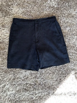 There glory days linneshorts i S - Mörkblå shorts i 100% linne ifrån there glory days. De är använda ca 5 gånger och har inga tecken på användning alls. De har sidofickor fram, två bakfickor med knapp och stängs med knapp och gylf framtill samt snörning på insidan. Perfekta för varma dagar och enkel att matcha med olika stilar.                                                                                      