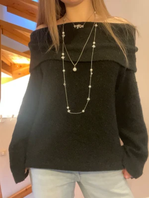 Svart off shoulder stickad tröja - Svart stickad tröja med off shoulder-design och bred krage. Tröjan har långa ärmar och en mjuk, lite luddig struktur som ger en mysig känsla. 
