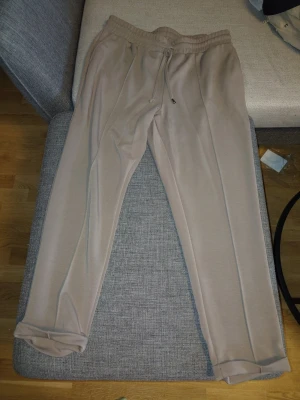Beige mjukisbyxor - Säljer ett par beige mjukisbyxor med resår i midjan. Byxorna har raka ben och är gjorda i ett mjukt, stretchigt material som känns riktigt bekvämt. Perfekta för chill dagar eller när du vill ha det extra comfy.
