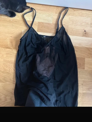 Svart linne mesh - Säljer ett svart nattlinne med tunna axelband och v-ringning. Nattlinnet har en liten rosett och spetsdetalj framtill, samt är gjort i ett tunt, lätt och något transparent material. Perfekt för mysiga kvällar hemma.