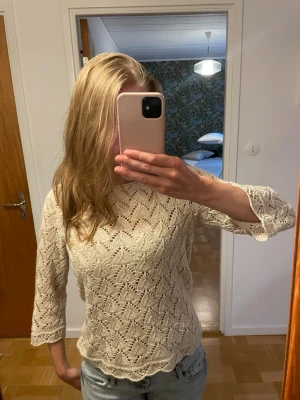Trekvartsärmad tröja - Säljer en beige stickad tröja med virkat mönster och trekvartsärmar. Tröjan har en rund halsringning och är hålig i materialet. 