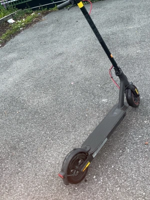 Svart elsparkcykel med röda detaljer - Elektrisk sparkcykel i svart med röda detaljer på kablarna och gula reflexer vid hjulen. Den har en lång, smal ståplatta och robusta däck. Perfekt för att ta sig fram snabbt i stan. Materialet är mestadels metall och plast.