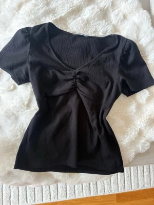 Svart ribbad topp från Vero Moda! <3 - Snygg, svart topp från Vero Moda med korta puffärmar och v-ringning. Toppen har en smickrande rynkning framtill och är perfekt att styla med jeans eller kjol.