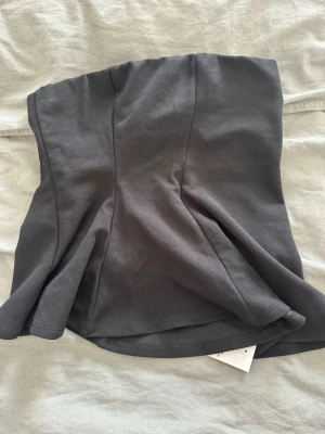 Svart bandeau peplum topp från Boohoo - Säljer en svart bandeau peplum topp från Boohoo. Toppen är axelbandslös och har en snygg utsvängd peplumform som ger en cool siluett. Perfekt att styla med jeans eller kjol för en trendig look.