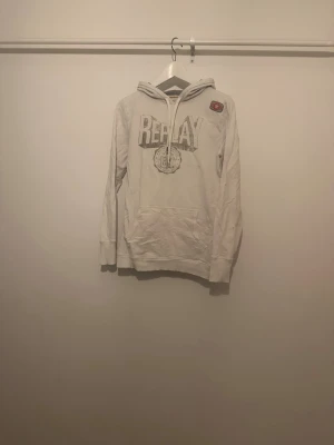 Vit hoodie med tryck från Replay - Snygg vit hoodie från Replay med stort tryck på bröstet. Mycket bra skick förutom 2st små svarta fläckar, Kankse kan få bort har ej försökt. Storlek S, killen på bilden är 184 och den är för liten.