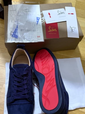 Mörkblåa sneakers från Louboutin - Snygga mörkblåa sneakers i mocka från Christian Louboutin med den ikoniska röda sulan. Skorna har rund tå, matchande mörkblå snörning och diskreta detaljer. Perfekta för dig som vill sticka ut med stilrena och exklusiva sneakers.