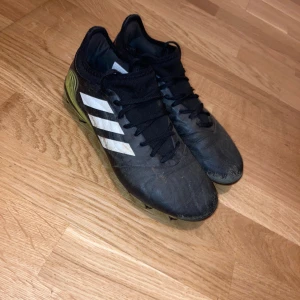 Copa Adidas Fotbollsskor - Säljer ett par använda svarta fotbollsskor från Adidas som funkar fortfarande lika bra o använda med vita ränder på sidan och limegröna detaljer vid hälen och under sulan. Skorna har snörning och platt sula med dobbar för gräsplan