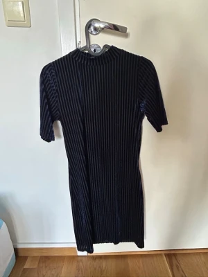 Mörkblå ribbad kortklänning - Säljer en mörkblå kortklänning med ribbad struktur och korta ärmar. Klänningen har en hög hals och är figurnära i modellen. Perfekt för dig som gillar enkel men stilren design.