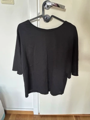 Svart topp med trekvartsärm från Ellos - En enkel svart topp från Ellos med rund halsringning och trekvartsärm. Tillverkad i ett mjukt och tunt material som känns skönt mot huden. Perfekt att styla med jeans eller kjol för en clean look.