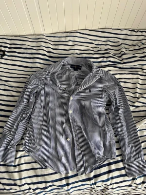 Randig skjorta från Ralph Lauren M - Riktigt fräsch skjorta från Ralph Lauren i vita och blåa ränder. Skjortan har lång ärm, knappar framtill och en tidlös krage. Tillverkad i mjuk bomull som känns skön mot huden. Perfekt för dig som gillar en clean och stilren look.