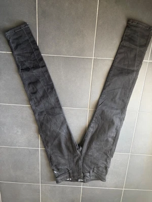Svarta replay anbass Jeans - Säljer ett par svarta replay anbass jeans med hög midja och smal passform hela vägen ner. Jeansen har klassisk femficksdesign och dragkedja med knapp framtill. Materialet är lent och skönt och sitter tight längs benen. Sitter tightare än 28x32 så skulle nog säga att storleken är 27x32. 