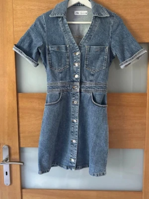 Jeansklänning från Zara - Säljer en snygg jeansklänning från Zara med kort ärm, v-ringning och knappar hela vägen framtill. Klänningen är endast andvänd 1 gång utan några defekter! Pris kan diskuteras vid snabbaffär!❤️🥰