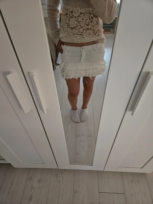 Vit jeanskjol med volanger - Säljer en vit jeanskjol med volanger och råa kanter. Kjolen har klassisk jeanslook med knapp och fickor fram. Perfekt för dig som gillar en söt och trendig stil. Skriv för mer bilder eller frågor.
