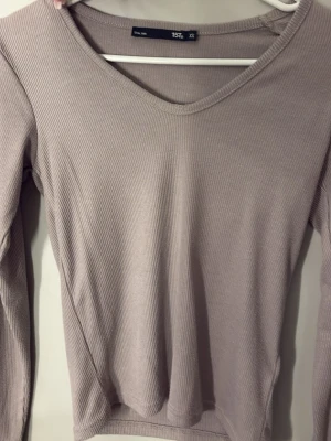 Beige ribbad långärmad topp  - Säljer en beige ribbad långärmad topp i storlek XS. Toppen har v-ringning och är tillverkad i ett mjukt, stretchigt material som sitter snyggt. Har även samma tröja i en grön färg, finns i min profil!