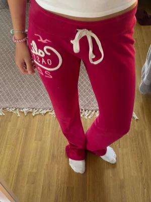 Rosa mjukisbyxor Hollister - Snygga rosa mjukisbyxor från Hollister med broderad logga fram och text bak. Byxorna har dragsko i midjan. Små vita fläckar på framsidan och på kanterna. Mjukt och skönt material i bomullsblandning.