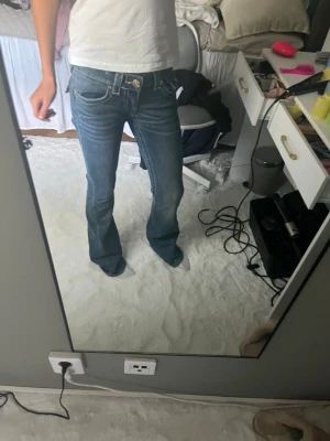 True religion jeans - Snygga blå bootcut jeans med låg midja och klassiska fickor fram och bak. Jeansen har en lätt utsvängd passform nertill och detaljerade sömmar vid fickorna. Perfekta för en avslappnad och trendig look.