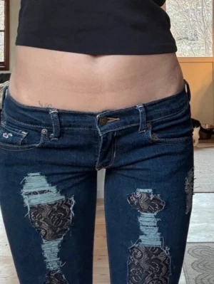 Hollister - Low Rise, Low Waist - Jeans Med Spets - Lågmidjade jeans från Hollister med spets och slitningar. Mycket bra skick, lite slitna på nederkant av benen. W26, L35 men osäker på om det fortfarande stämmer då de är omsydda. De är utsydda nedtill för att de ska bli flare/bootcut. Köpta tidigare på Vinted men säljer då de inte passade. Skriv privat för bilder med dem på. Mått: Midja: 37x2cm, Höfter: 40x2cm, Lårbredd ~20x2cm, Benlängd utsida: 99cm, Benlängd insida: 83cm, Midjehöjd från skrevet: 18cm, Bredd längst ner: ~23x2cm