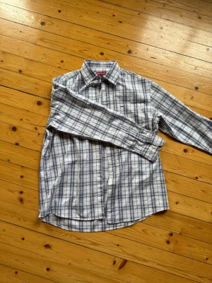 Rutig skjorta från Redwood L - Klassisk rutig skjorta från Redwood i vitt, blått och grått. Skjortan har lång ärm, knappar framtill och en avslappnad passform. Perfekt för dig som gillar en tidlös stil med lite edge.