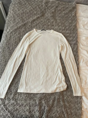 Vit långärmad topp från Zara - En enkel och stilren vit långärmad topp från Zara. Tillverkad i ett mjukt och tunt material som känns skönt mot huden. Perfekt att styla med jeans eller kjol för en clean look.