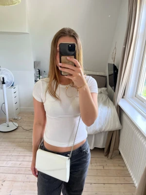 Vit kuvertväska med kedja - Snygg vit kuvertväska med silverfärgad kedjerem. Kan användas som en clutch också. Har några bronzer fläckar inuti väskan 