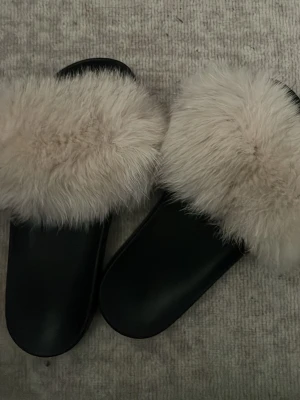 Svarta sandaler med fluffig päls - Säljer ett par svarta sandaler med breda remmar täckta av mjuk, beige fluffig fuskpäls. Snygg slip-in modell som ger en trendig och cozy vibe. Perfekta för att lyfta vilken outfit som helst med lite extra attityd. Det finns även i andra färger ☺️
