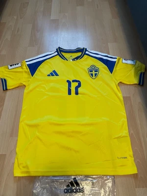 Sverige matchtröja Adidas nr 17  - Gul matchtröja från Adidas för svenska landslaget med blå detaljer, nummer 17 och namnet Gyökeres på ryggen. Tröjan har korta ärmar, broderad landslagssköld och Climacool-material för bra ventilation. Perfekt för fotbollsfans!