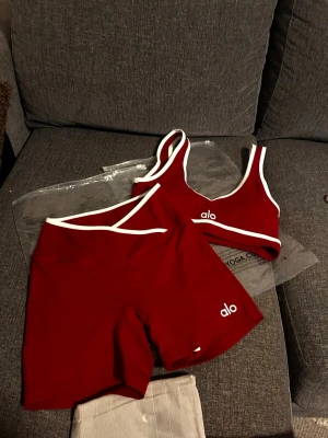 Rött sportigt set - Snyggt rött set med vita detaljer. Setet består av en sport-bh och matchande shorts, båda med vit kant och logga. Materialet är stretchigt och mjukt, perfekt för träning eller chill. Modern och sportig look.