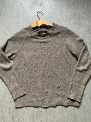 Beige stickad tröja från Vero Moda - Mysig beige stickad tröja från Vero Moda med rund halsringning och långa ärmar. Tröjan har en enkel och stilren design med ribbstickade muddar vid ärmslut och nederkant. Perfekt för lager på lager och passar till det mesta.
