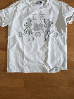 Vit t-shirt med tryck - Vit t-shirt med ett stort tryck framtill i silver med två figurer, 