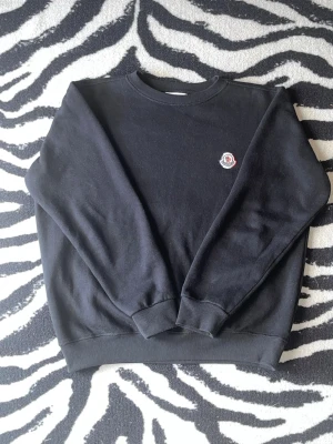 Moncler Sweater - Svart stickad tröja från Moncler med rund halsringning och ribbade muddar. Tröjan har en liten Moncler-logga broderad på bröstet. Perfekt för dig som gillar stilrena och klassiska plagg.