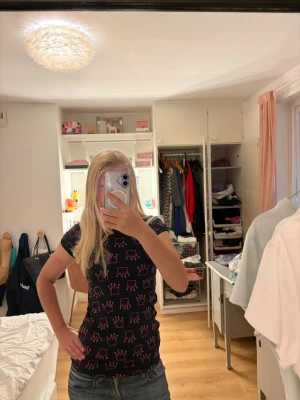 Svart t-shirt med rosa kronmönster - Snygg svart t-shirt med korta ärmar och rosa kronmönster över hela tröjan. Skulle säga storlek XXS eller XS
