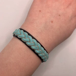 Tenntrådsarmband  - Handgjort Tenntrådsarmband, svart med blå fläta. Materialet armbandet är gjort i är lammskinn, och flätan är gjort i tenntråd. Armbandet kan hålla i flera år. Om du har någon fråga kan du gärna skriva en kommentar eller meddela mig.