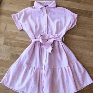 50-tal klänning  - En ljusrosa och vit randig klänning med 50-tal vibes. Storleken är S men liten i storlek så skulle säga XS💓 skicket är begagnat och tyget ganska tunt. Det finns minimala defekter, exempelvis lite sliten tråd runt knapparna samt små hål i ryggen (se sista bilden). OBS bandet är oknutet på bilden och går att ta av 